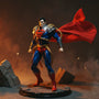Wired deep red cape with gold trim on action figure torso on cracked concrete base with red-yellow backlight and city skyline
