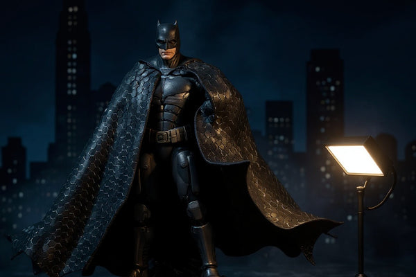 McFarlane Batman figures with fabric capes displayed on a rooftop diorama with a glowing Bat-Signal against a Gotham skyline backdrop, lit with moody blue light.