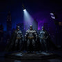 Batman Ultimate Movie Collection 6-pack action figures displayed on a miniature Gotham City skyline backdrop with Bat-Signal spotlight, dramatic blue and purple lighting.