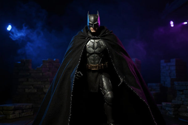 Dark charcoal-black matte fabric cape with wire-frame ridges draped over a medieval-armored Batman figure, posed before a gothic castle backdrop with blue and purple uplighting, stone ruins, and fog.