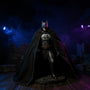 Dark charcoal-black matte fabric cape with wire-frame ridges draped over a medieval-armored Batman figure, posed before a gothic castle backdrop with blue and purple uplighting, stone ruins, and fog.