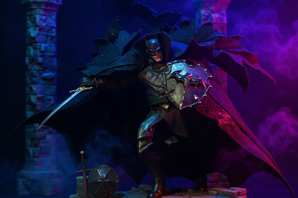 Dark charcoal matte fabric cape with wire-frame ridges draped over medieval-armored Batman action figure against gothic castle backdrop with blue purple LED fog.
