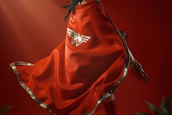 Dynamic fabric cape in earthy red and brown, draped with internal wire posing, against a bold amber-to-crimson gradient background with jungle props and fog.