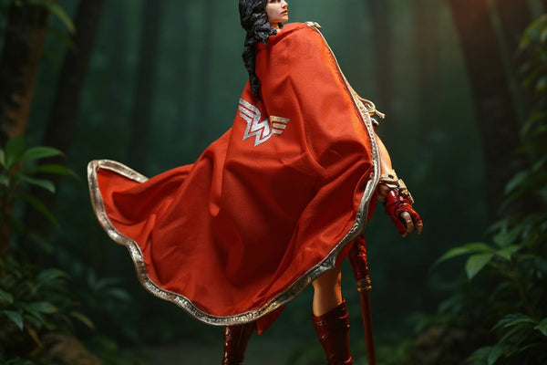 Shapeable wire fabric cape in deep red and tan draped on a 7-inch female warrior action figure, posed on rocky jungle diorama with spear and foliage.