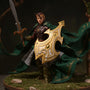 Flowing dark green and brown fabric cape on an action figure in a fantasy forest diorama with moss, rocks, and a bow, wrapped in warm directional light and fog.