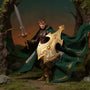 A dark green and brown fabric action figure cape with wire-shaped folds, draped over a small fantasy figure's shoulders, set in a miniature forest diorama with moss and rocks, under dramatic warm lighting.