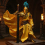 Golden metallic fabric cape on a 1/12 scale armored knight action figure, posed dynamically in a miniature medieval castle diorama with torches and stone pillars.
