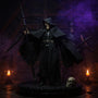 Dark textured fabric cape with visible seams and wire-enhanced drape flowing over a black display platform, surrounded by miniature skulls and bones, fog, and candlelight against a deep violet and blue gradient background.