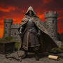 Soft fabric cape in weathered brown-tan hues billowing on a 1/12 scale crusader archer figure against a dramatic medieval stone castle backdrop with bright crimson-amber gradient sky, wooden crate, moss rock, and bow prop.