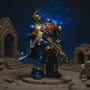 Handmade deep blue cloth cape with gold trim and parchment purity seal draped over a 1/18 action figure shoulder, posed dynamically on a miniature battlefield diorama with rubble and bolter rifle, dramatic blue and gold lighting.