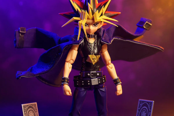 Dark purple wired fabric cloak with visible stitching draped on a small anime action figure, surrounded by miniature dueling cards and a millennium puzzle, against a bold purple and gold gradient background.