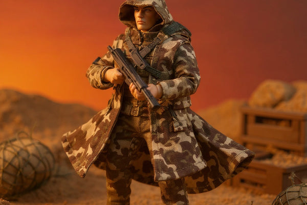 Handmade miniature camo coat and pants set on a 1/12 action figure in a desert diorama with sandbags and crates.