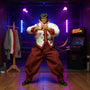Handmade soft cloth costume with bendable wire hems draped on a tiny mannequin stand in a miniature dojo, surrounded by neon-lit arena props, fabric swatches, and sewing spools, against a bold blue to magenta gradient background.