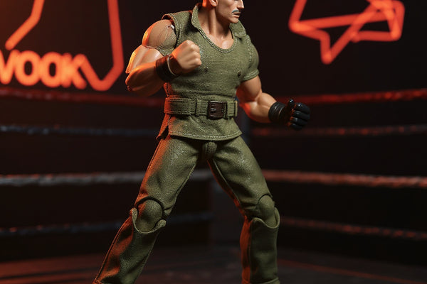 1/12 scale khaki military fabric outfit on a headless articulated figure frame, staged in a fighting game arena diorama with tactical props and arcade cabinet backdrop.