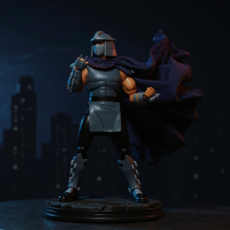 Black fabric cape with red trim on Shredder figure, posed on a rooftop diorama with neon city backdrop and dramatic lighting.