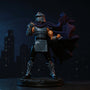 Black fabric cape with red trim on Shredder figure, posed on a rooftop diorama with neon city backdrop and dramatic lighting.