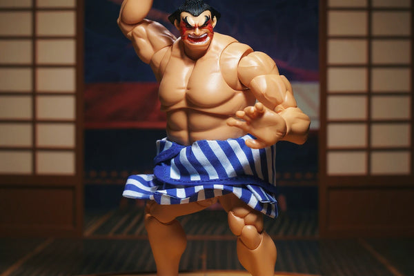 Blue cloth mawashi belt on a 1/12 scale action figure torso displayed on a miniature sumo ring platform with a Japanese folding screen in the background under dramatic lighting.