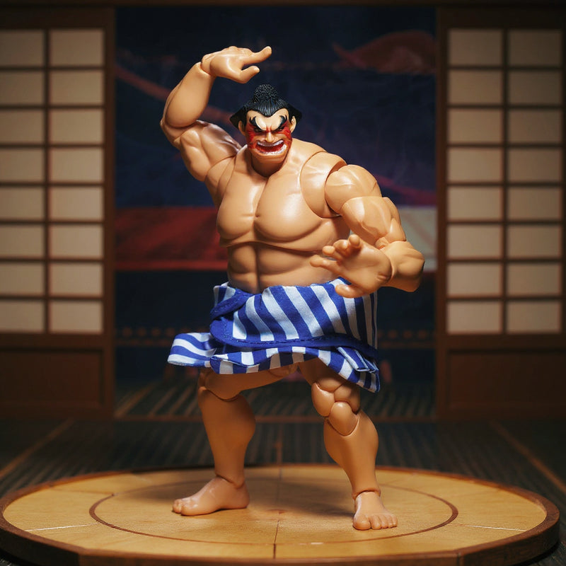 Blue cloth mawashi belt on a 1/12 scale action figure torso displayed on a miniature sumo ring platform with a Japanese folding screen in the background under dramatic lighting.