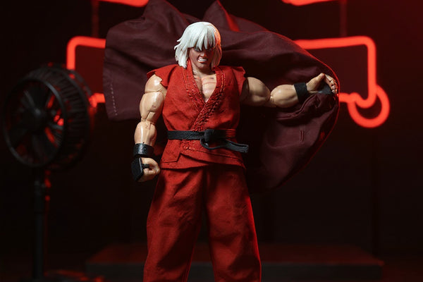 Miniature 1/12 scale wired cloth cape in dark red draped dynamically on a display stand against a neon arcade backdrop, with dramatic red rim lighting.