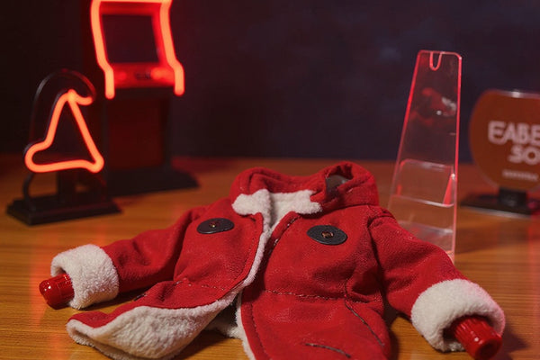 Red fabric military-style action figure jacket laid flat on a collector desk with miniature dojo backdrop and neon arcade signs.