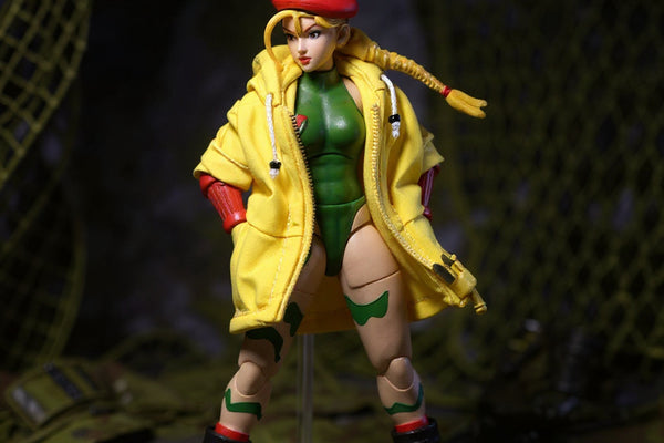 Bright yellow 1/12 scale military cropped jacket displayed on clear hanger in military diorama with camo netting, miniature combat boots and tactical gloves.