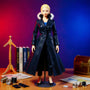 Dark navy-black long coat with fur-like collar and flared wire-structured silhouette draped on a faceless mannequin stand, surrounded by sewing tools, manga volumes, and pirate props against a vivid magenta-blue gradient background.