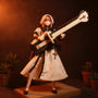 Miniature 1/12 scale cloth outfit with layered skirt and top in muted natural tones on a figure, displayed on a wooden shelf with potted plants against a bold gradient background.