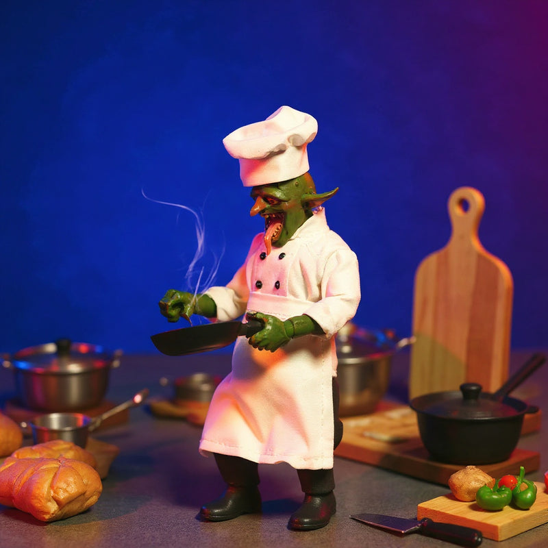 Miniature chef costume laid flat on a miniature kitchen counter with tiny utensils and food props, bold blue and magenta gradient background.