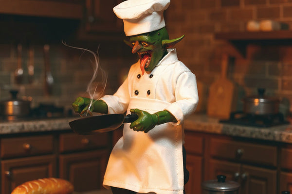 Miniature white chef jacket, apron, and small hat on a mohawk goblin figure in a bold miniature kitchen scene.