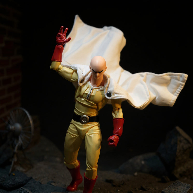 Yellow-and-white fabric action figure cape billowing on a mannequin torso against a bold rooftop diorama with dramatic lighting