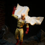 Yellow-and-white fabric action figure cape billowing on a mannequin torso against a bold rooftop diorama with dramatic lighting