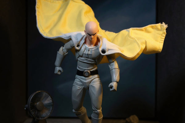 Yellow-and-white cloth cape on mannequin torso on urban rooftop diorama with wind effect and dramatic lighting.