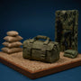 1/12 scale olive drab tactical duffel bag with visible stitching on sandbag barricade diorama with weapon rack and camo netting, vibrant blue gradient background