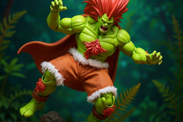 Soft fabric cape with wire-edged flowing drape on 1/12 action figure in jungle diorama with rocks and moss, high-contrast lighting.